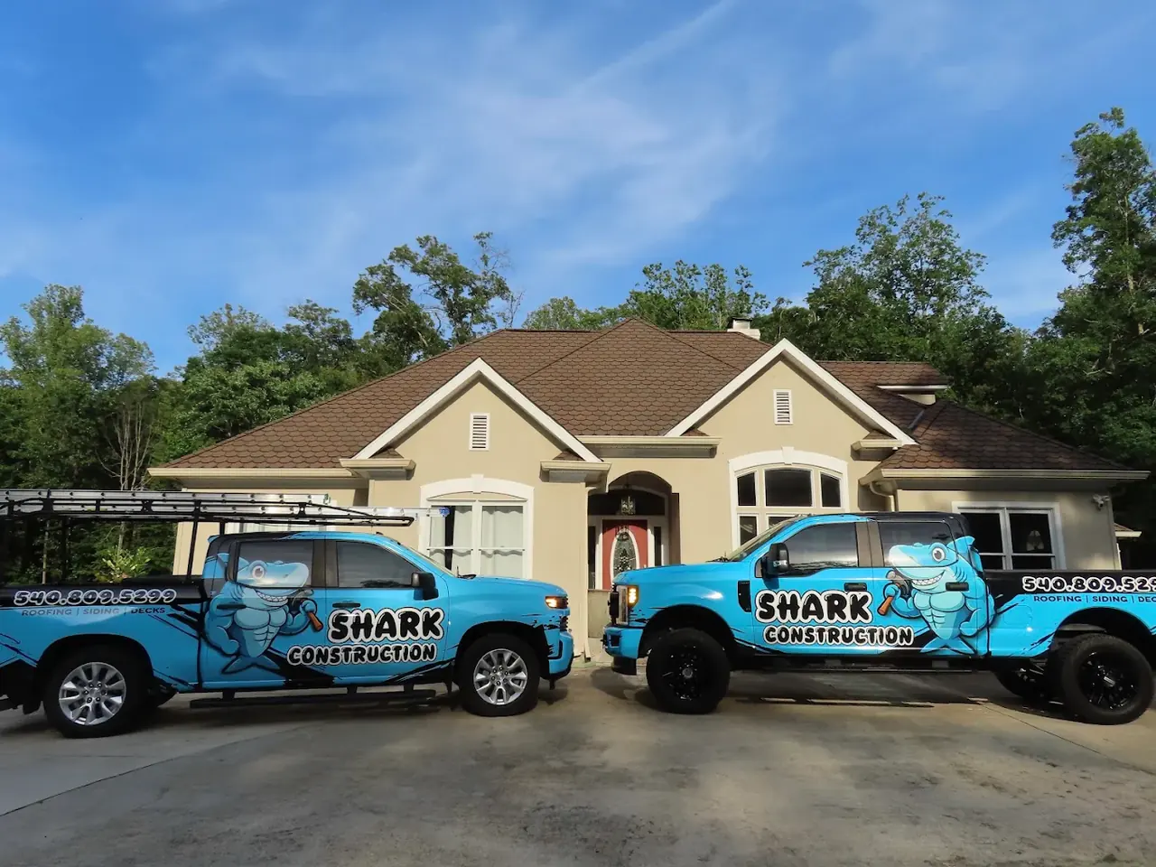 Two Shark Construction trucks parked in front of a completed shingle roof project in the Fredericksburg area